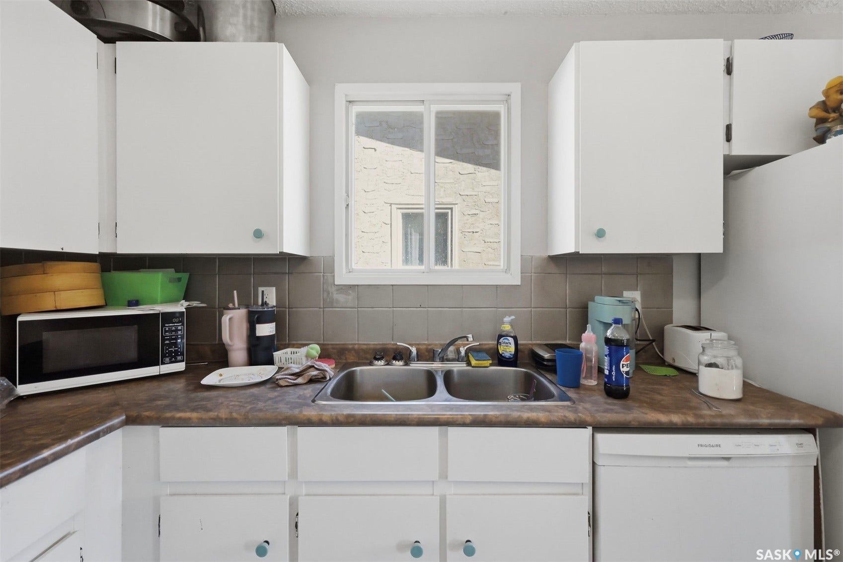White cabinetry with circular knobs, laminate countertops, tile backsplash, stainless steel double-basin sink, and a built-in dishwasher