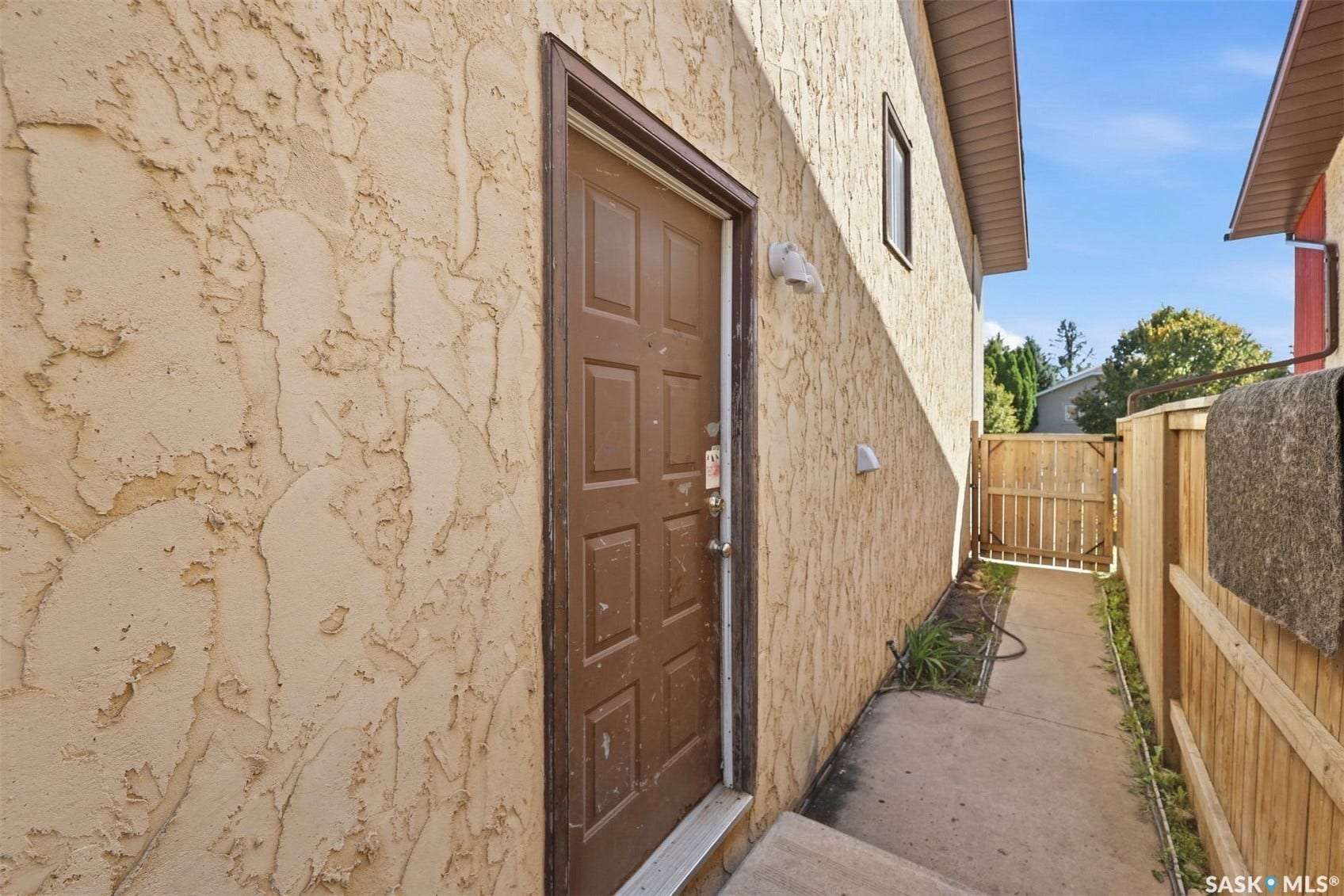 Textured exterior siding, paneled entry door, pathway access, wood fencing, and exterior lighting fixtures