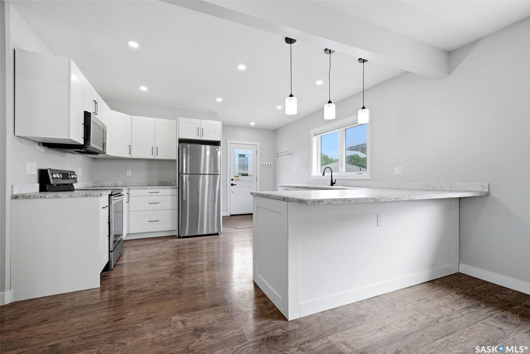 1601 Lacon Street, Regina SK S4N 1Z5 Kitchen featuring white cabinetry, stainless steel appliances, a light-toned countertop, wood-finish flooring, and pendant lighting over a kitchen island