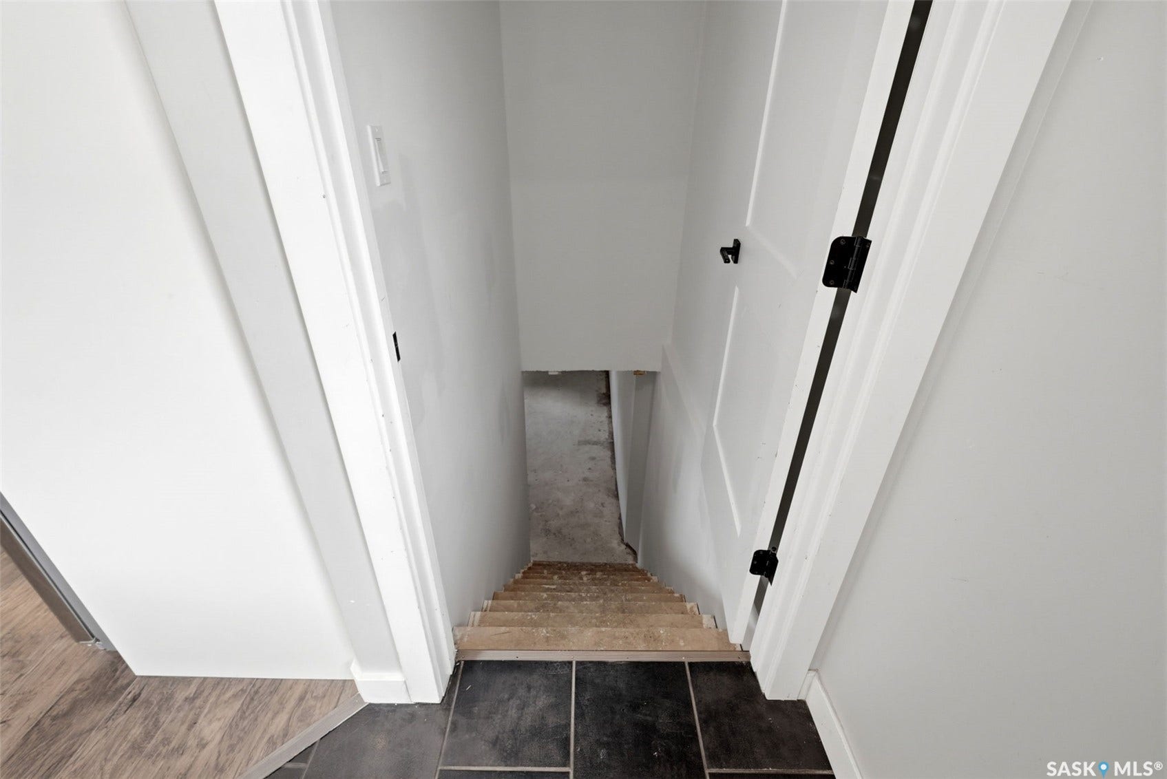 1601 Lacon Street, Regina SK S4N 1Z5 Wood-finish flooring, dark tile flooring, white interior walls, white door with dark hardware, and unfinished wood stairs