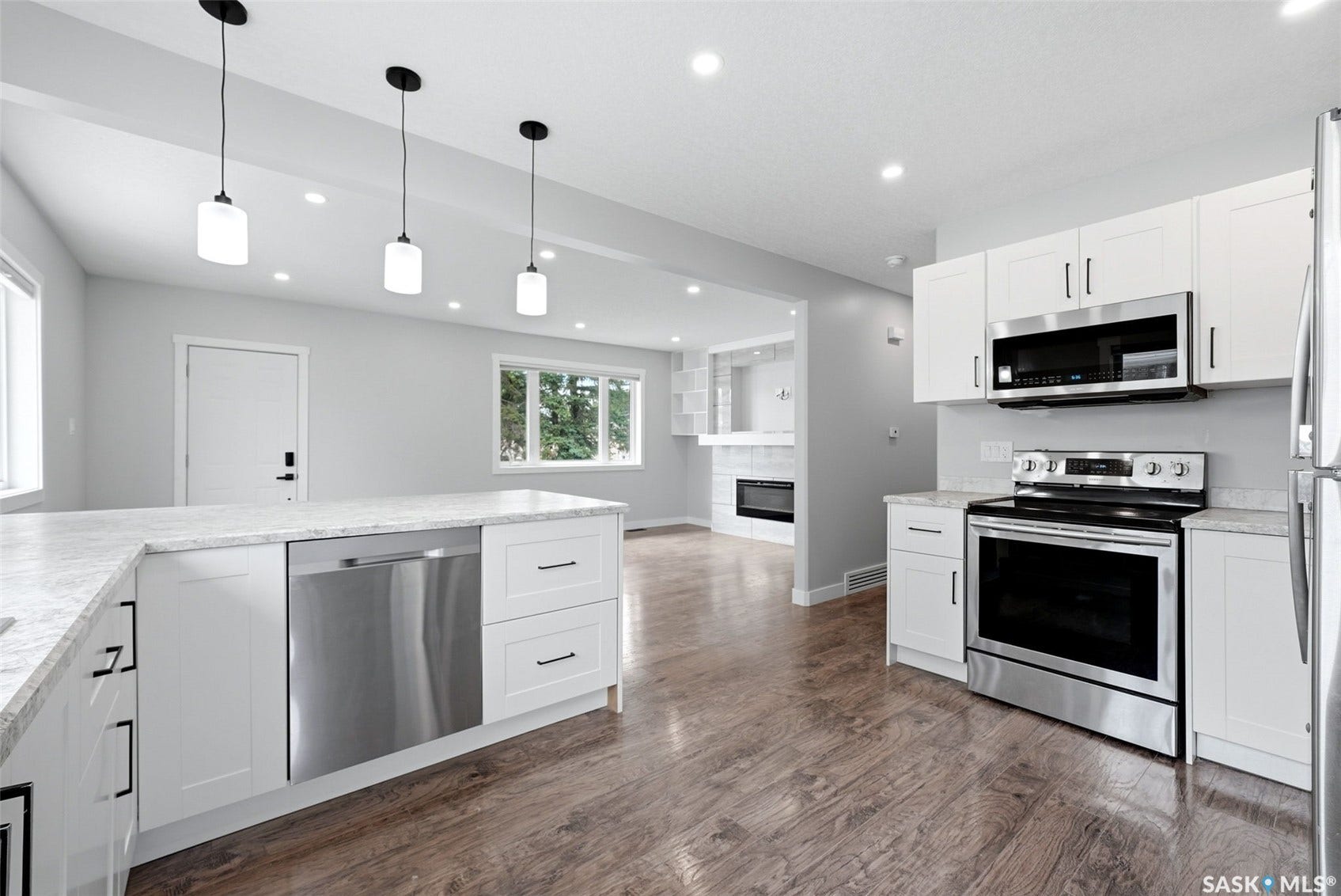 1601 Lacon Street, Regina SK S4N 1Z5 Kitchen featuring white cabinetry, stainless steel appliances, pendant lighting, wood-finish flooring, and a built-in electric fireplace in the background
