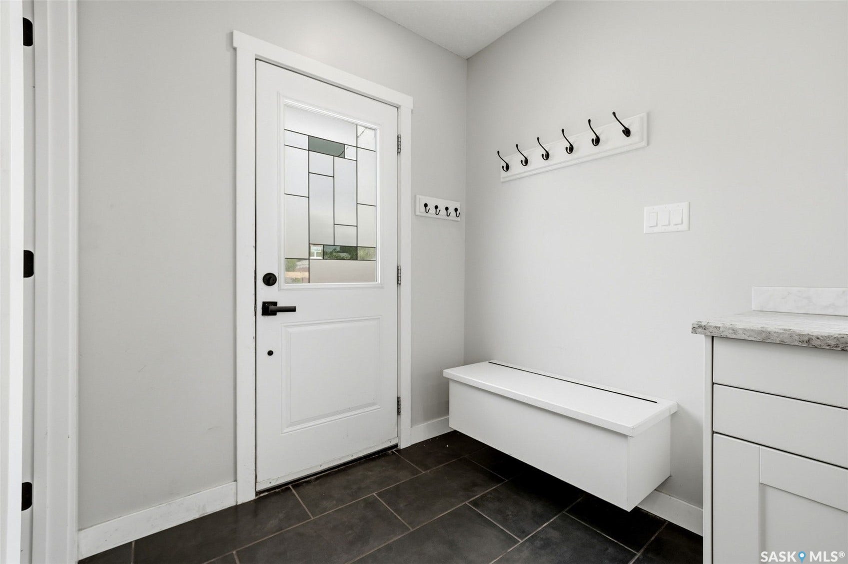 1601 Lacon Street, Regina SK S4N 1Z5 Entry door with decorative glass inlay, dark tile flooring, built-in storage bench, and white cabinetry with a light-toned countertop