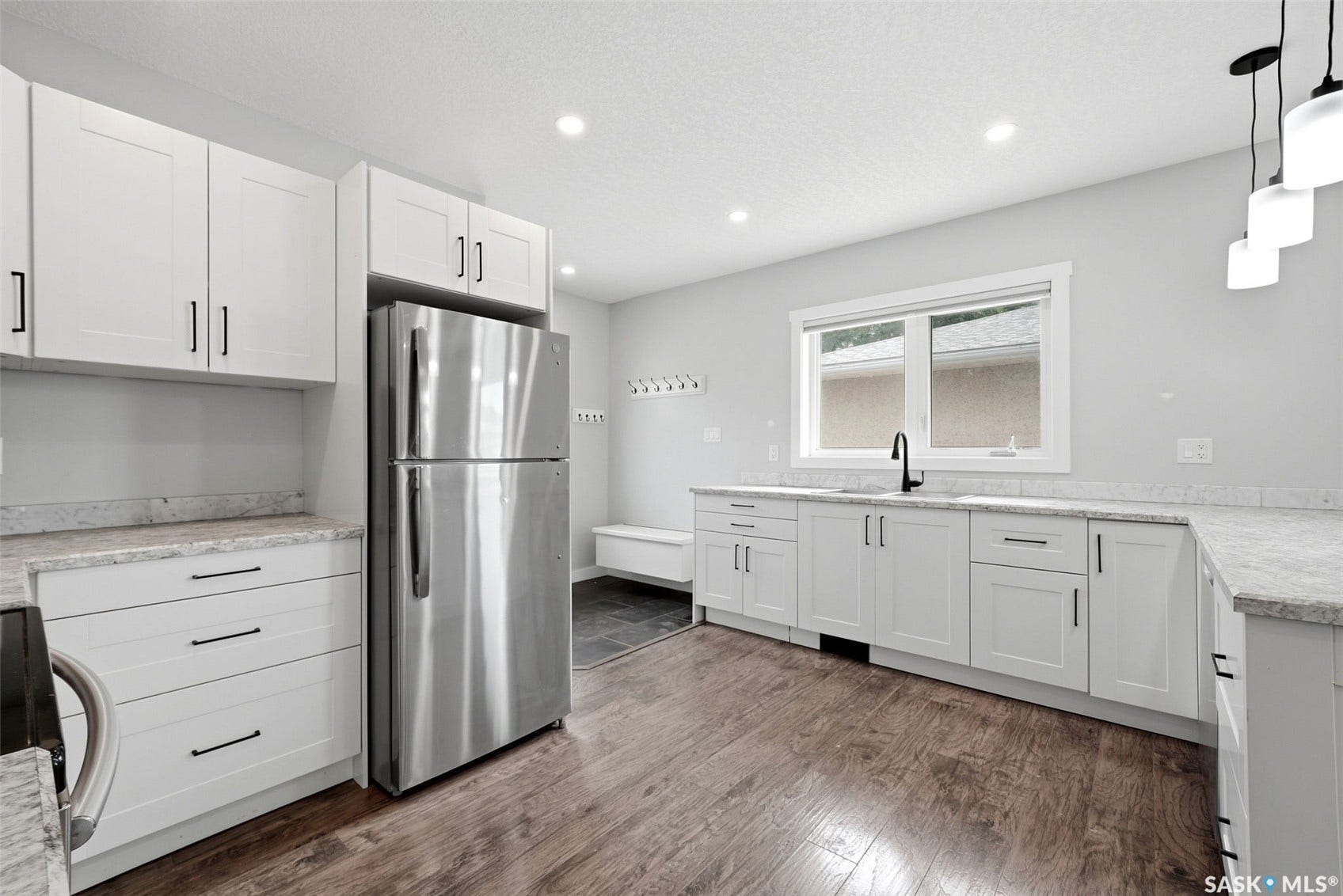 1601 Lacon Street, Regina SK S4N 1Z5 White shaker-style cabinetry with matte black hardware, stainless steel refrigerator, light-toned countertops, wood-finish flooring, and recessed lighting