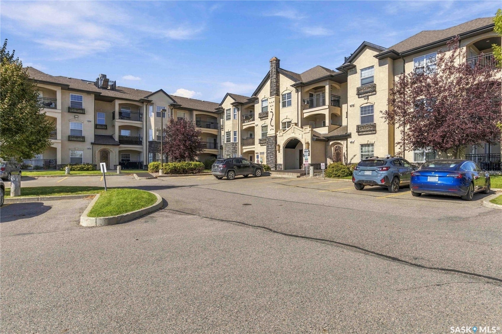 Multi-story building featuring a stucco exterior, stone accents, multiple balconies with dark railings, and a prominent arched entryway