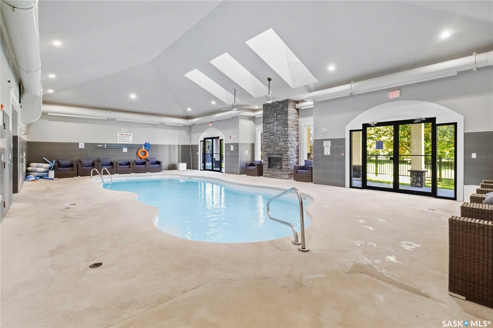 Indoor swimming pool featuring a curved freeform design, a stone-clad fireplace, vaulted ceilings with skylights, recessed lighting, and expansive glass doors