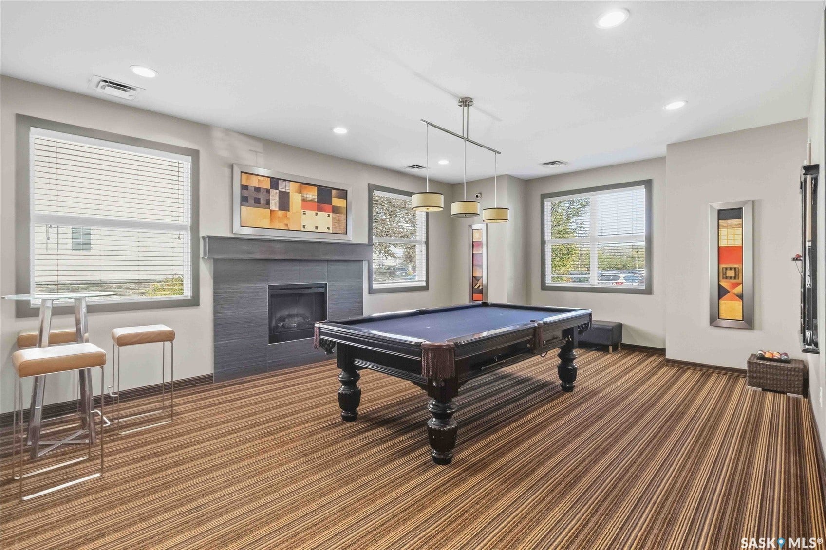 Room featuring a fireplace with a dark surround, multiple windows with blinds, recessed lighting, and a linear pendant light fixture