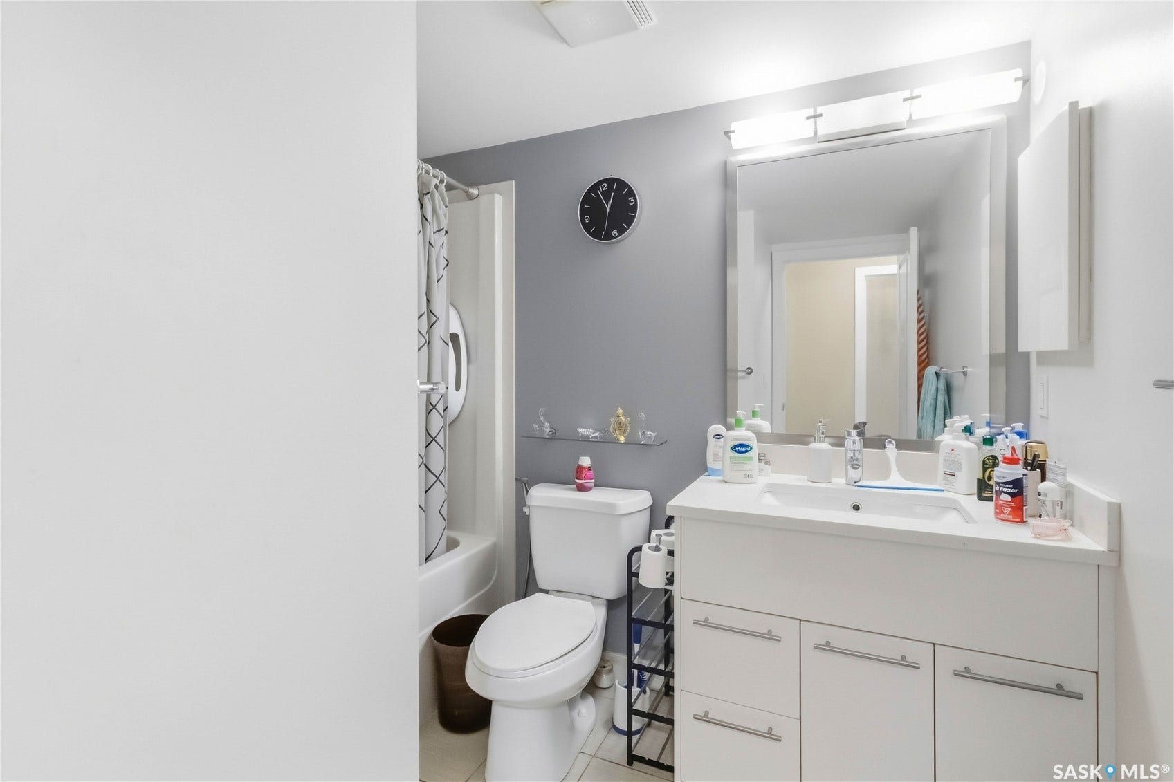 White vanity with a single basin sink, wall-mounted mirror, and overhead strip lighting