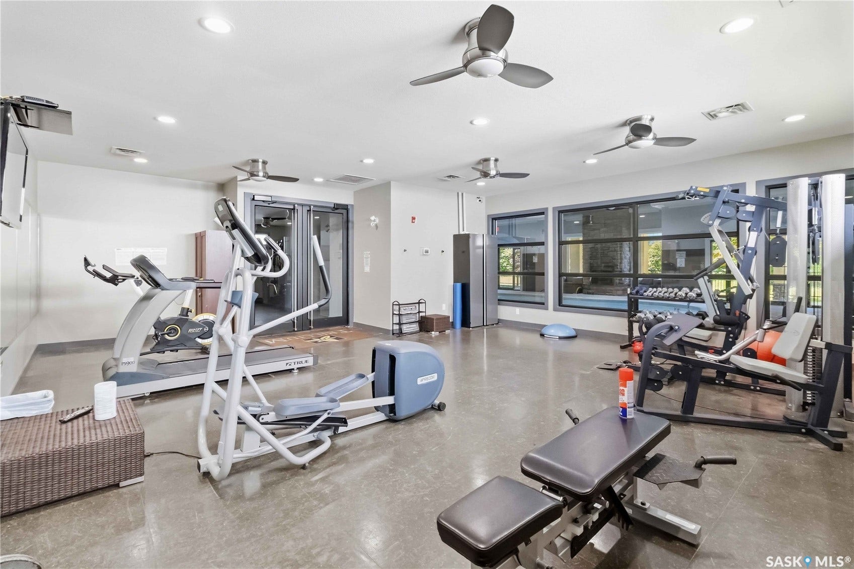 Spacious fitness area featuring multiple ceiling fans, recessed lighting, expansive windows, and durable flooring