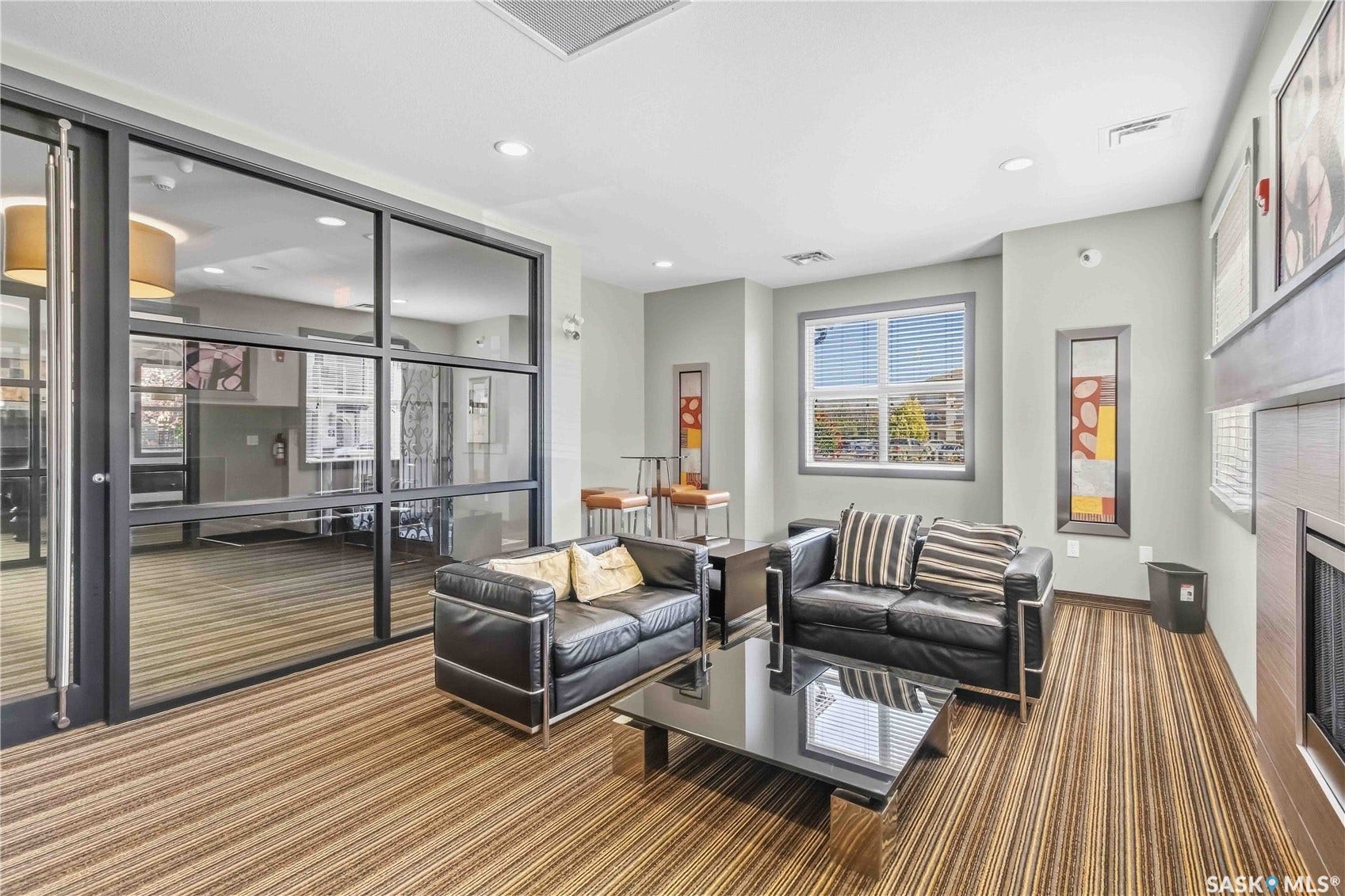 Spacious communal room featuring striped wood-finish flooring, a contemporary fireplace, large picture windows, and recessed lighting