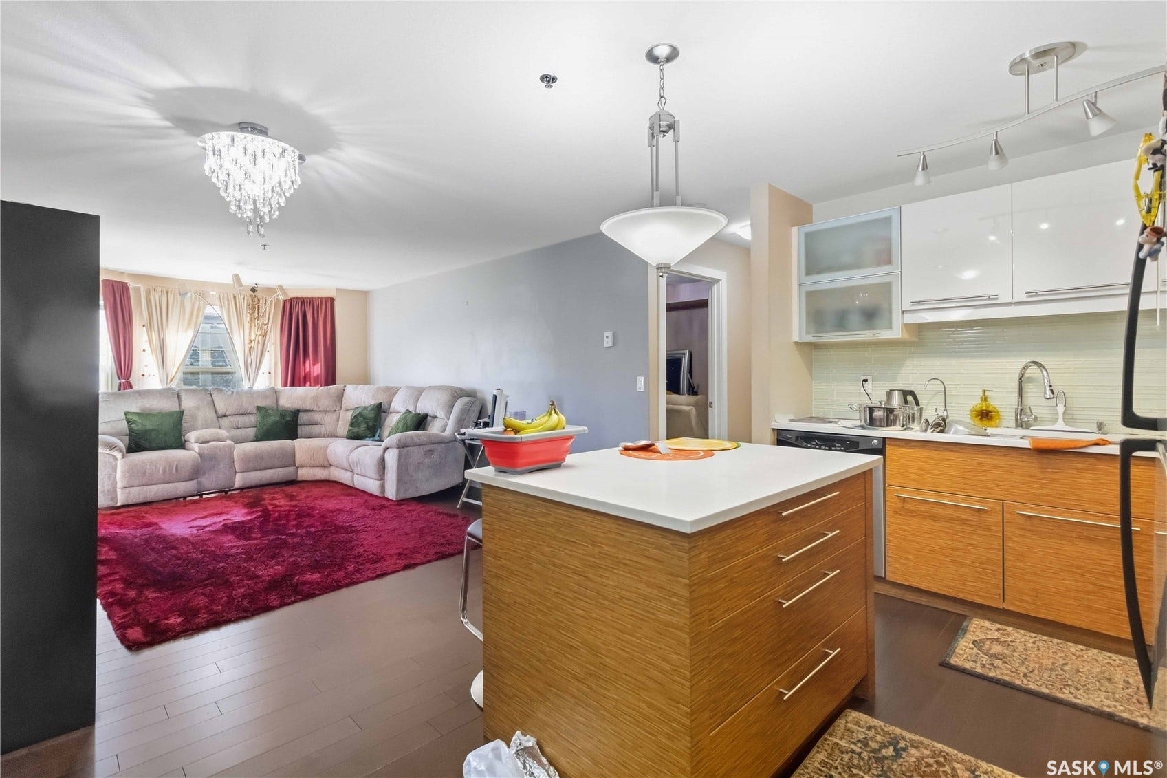 Open-concept living area featuring wood-finish flooring, a contemporary kitchen island with a light-toned countertop, white upper cabinetry, and wood-finish lower cabinetry