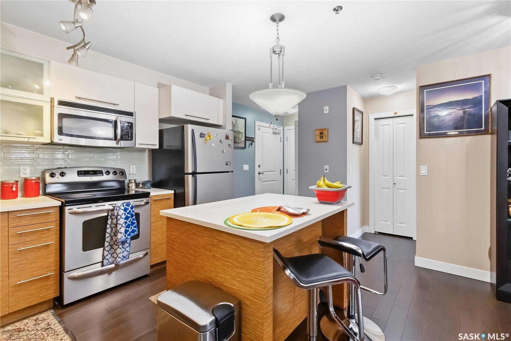 Kitchen featuring stainless steel appliances, wood-finish flooring, a central island with a light-colored countertop, and a tiled backsplash