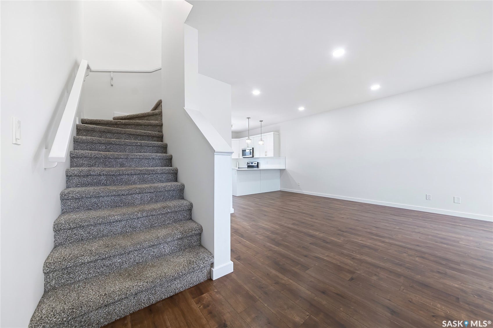 Carpeted staircase with white handrail, wood-finish flooring, recessed lighting, and white walls