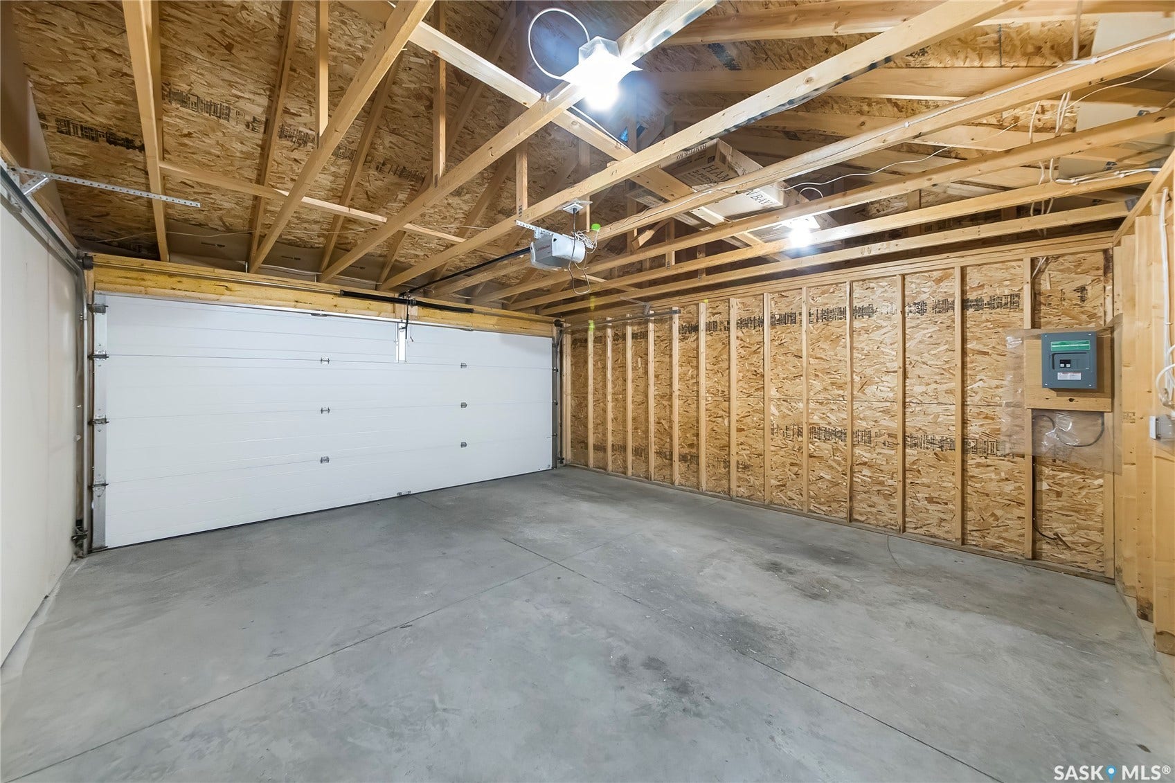 Concrete flooring, exposed wood framing, and a white paneled garage door