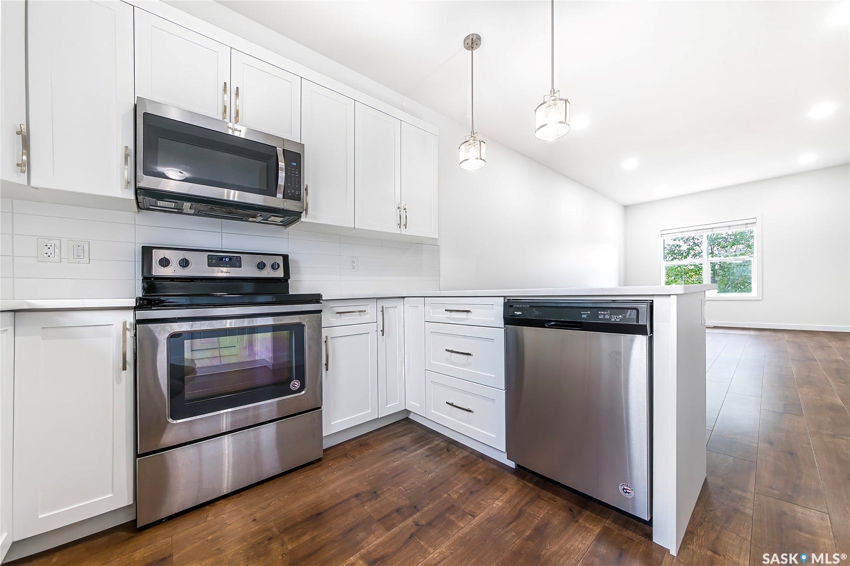 Kitchen featuring white shaker cabinetry, stainless steel appliances, light-toned countertops, wood-finish flooring, and pendant lighting