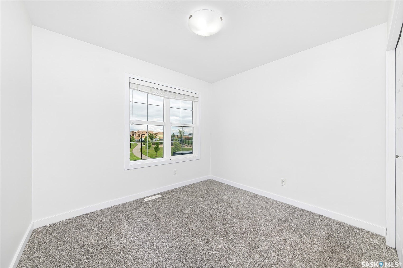 Neutral wall finishes, window with grids, overhead flush mount light fixture, and grey carpet flooring