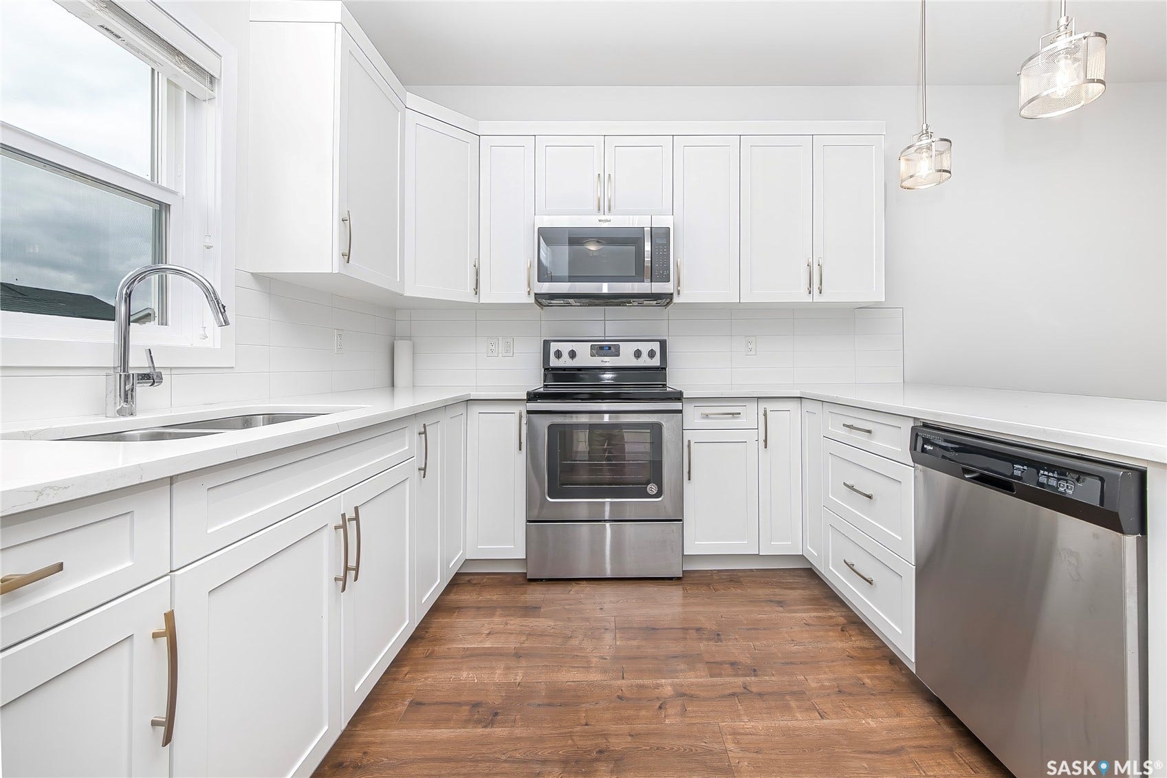 White cabinetry, stainless steel appliances, white countertops, subway tile backsplash, and wood-finish flooring