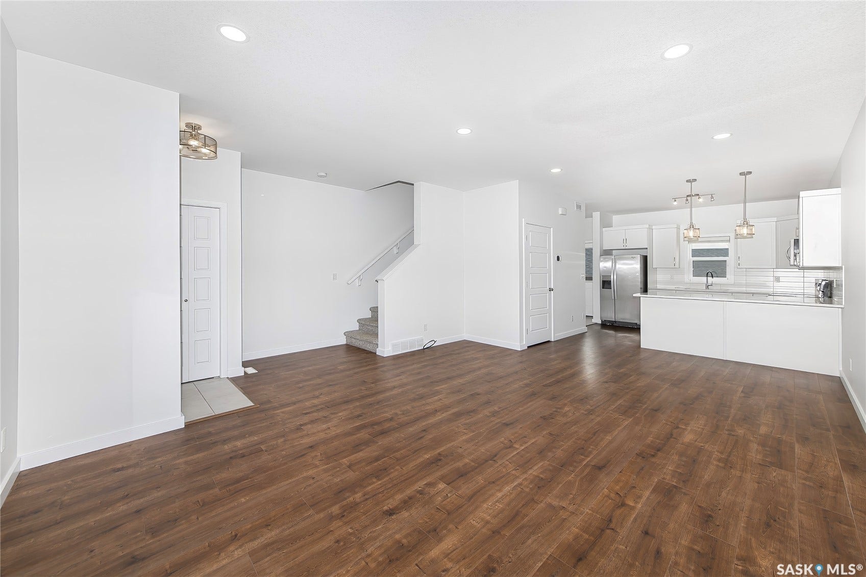 Wood-finish flooring, recessed lighting, white walls, white kitchen cabinetry, and stainless steel appliances