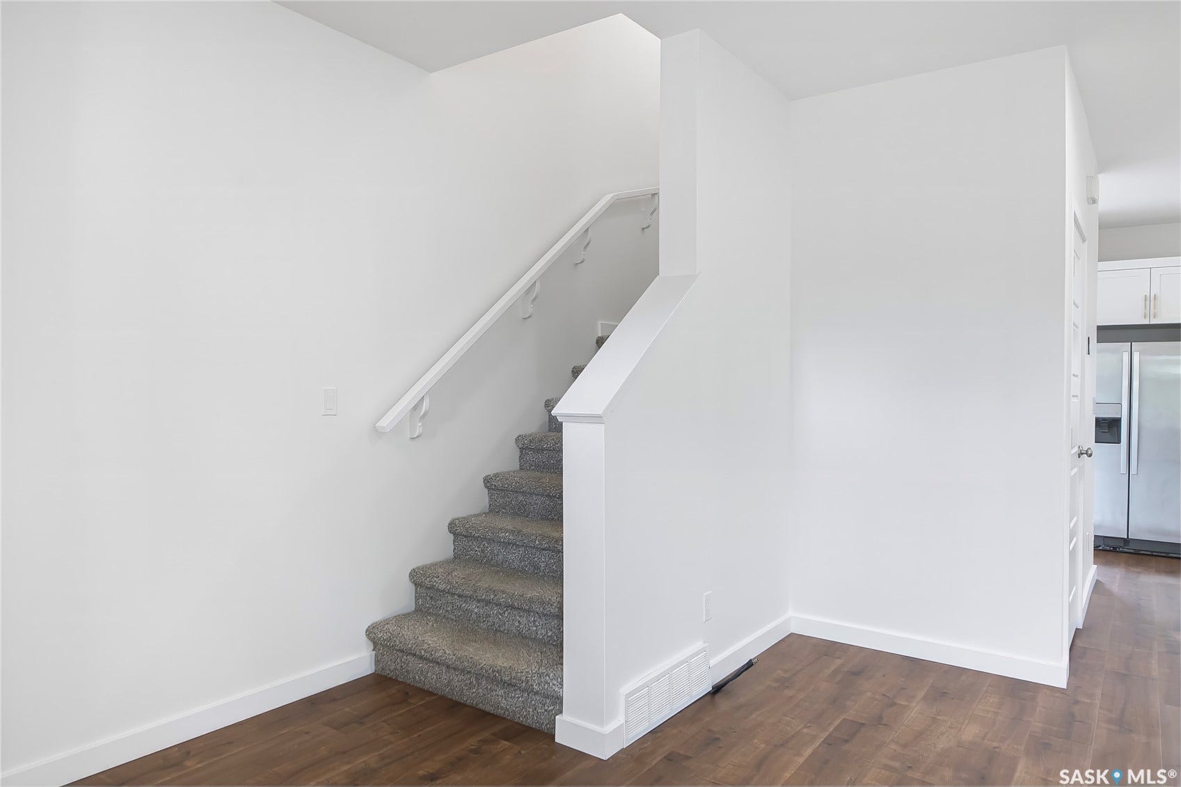 Interior staircase with carpeted treads and a white handrail, complemented by wood-finish flooring