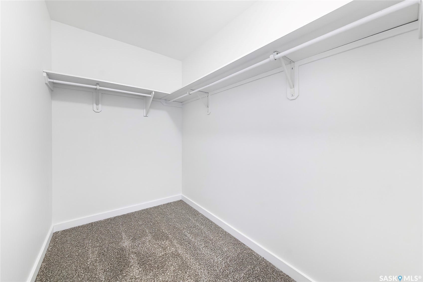 Walk-in closet featuring white walls, gray textured carpet, and L-shaped wire shelving with hanging rods