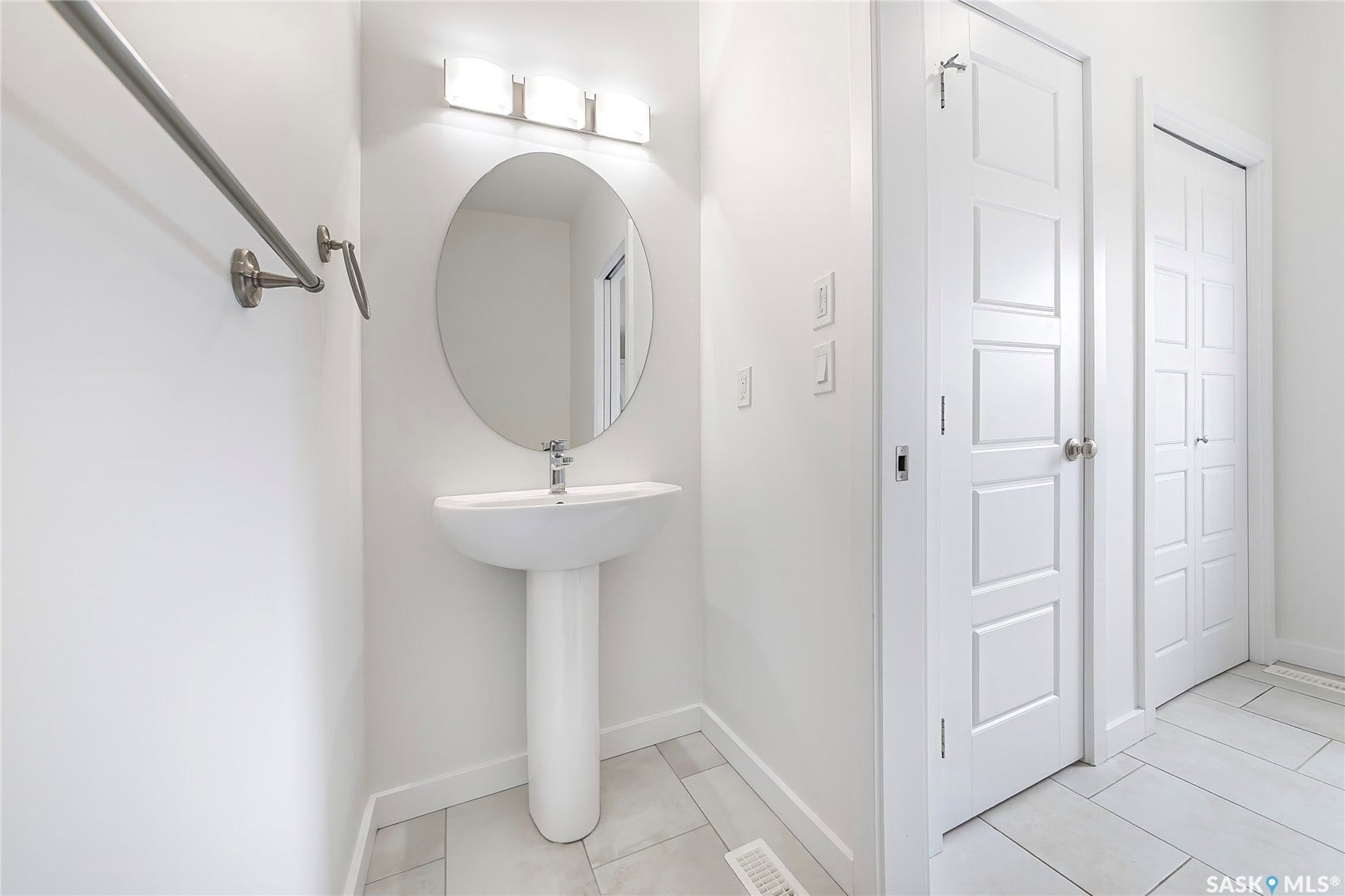 Pedestal sink with single-handle faucet, oval mirror, wall-mounted lighting fixture, and paneled interior doors
