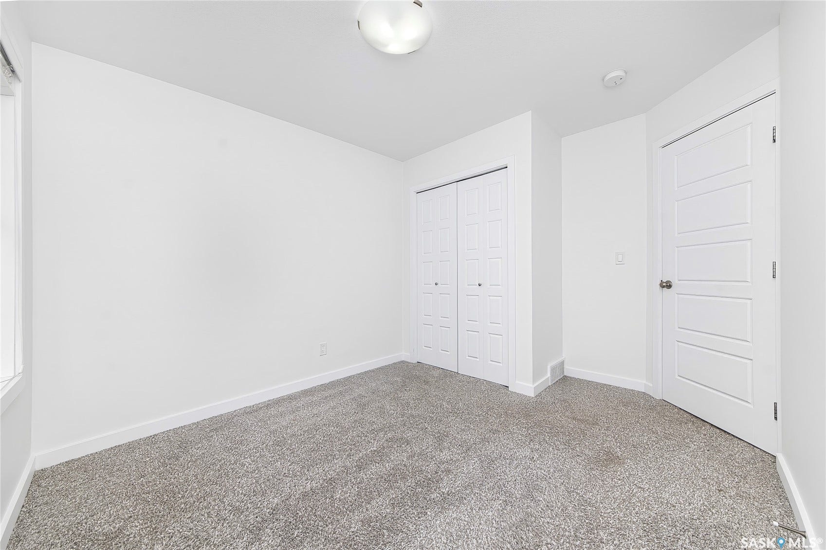 Neutral wall finish, grey carpeting, flush mount ceiling lighting, and a paneled door
