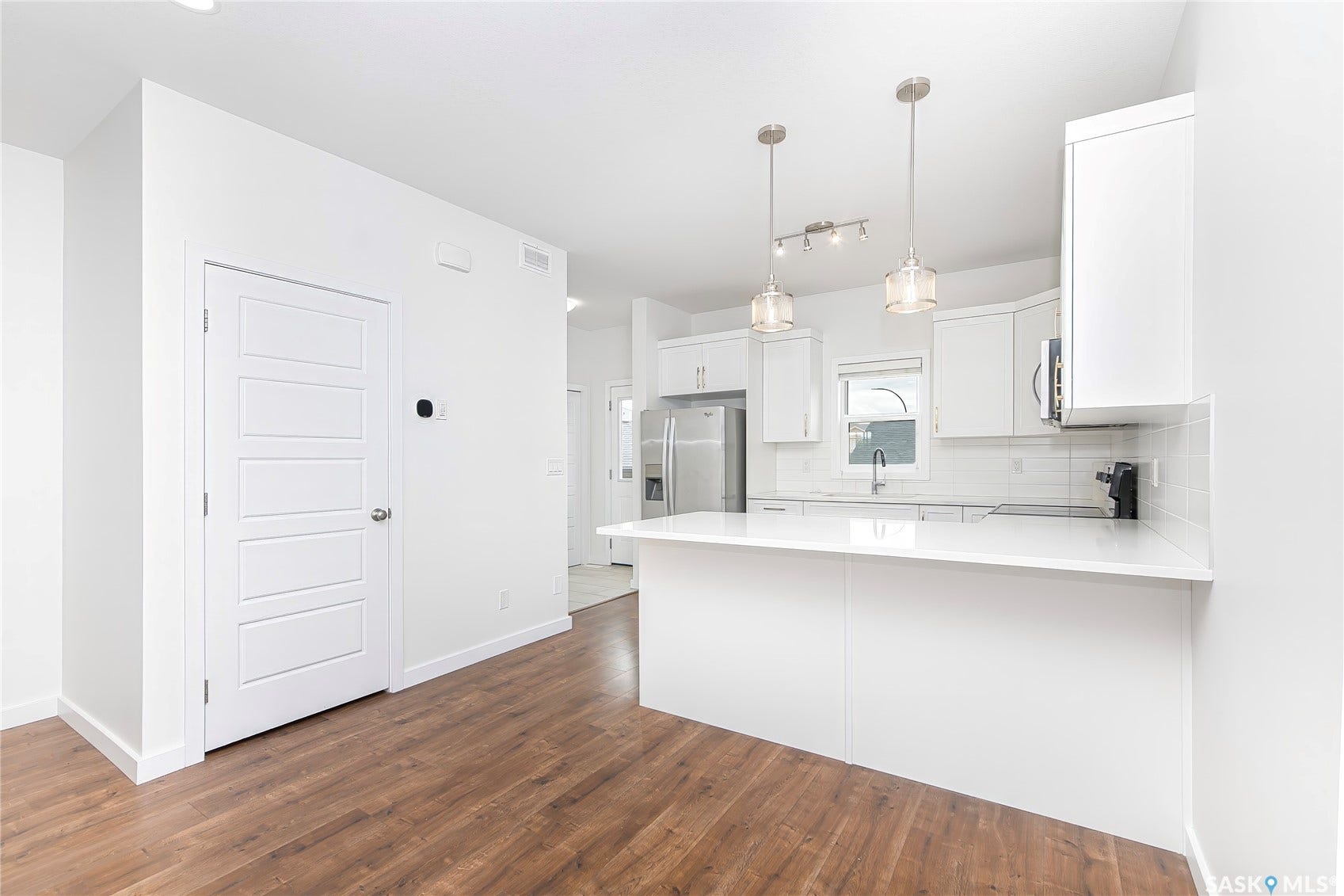 Open-concept kitchen featuring white cabinetry, stainless steel appliances, a white subway tile backsplash, and a breakfast bar with pendant lighting