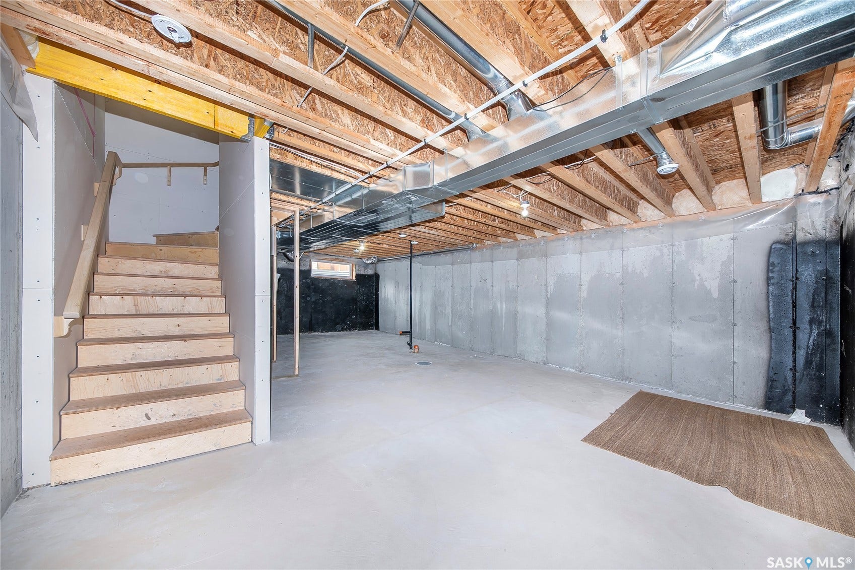 Unfinished basement with concrete flooring, exposed wooden joists, and a partial staircase