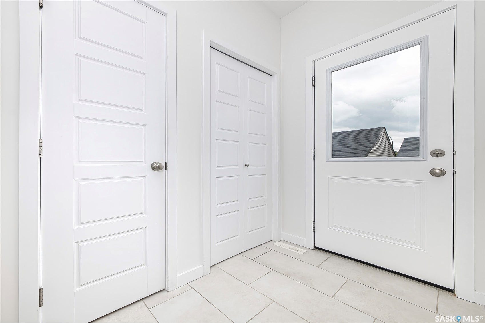 White interior doors, white paneled bifold closet door, white entry door with glass insert, light-toned tile flooring