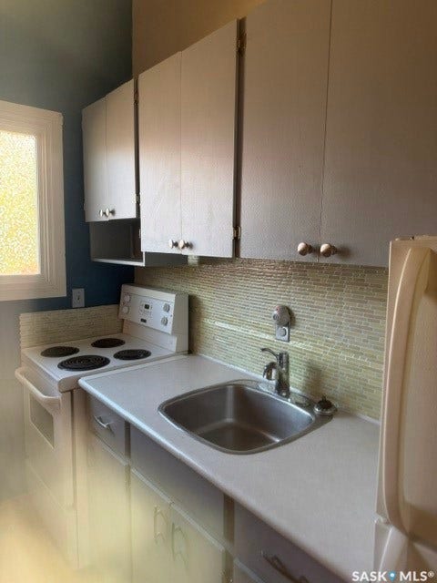 White cabinetry with silver-tone hardware, stainless steel sink, mosaic tile backsplash, and white range