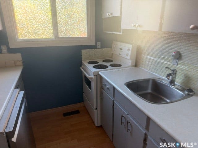 Kitchen featuring a white electric range, stainless steel sink, light-toned wood-finish flooring, and upper and lower cabinetry
