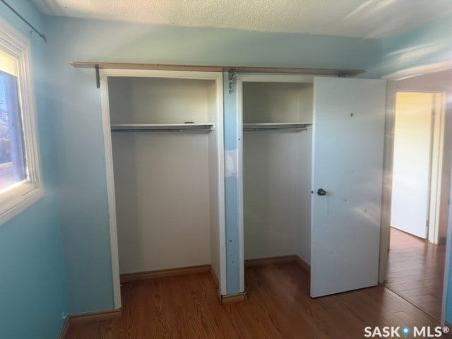 Wood-finish flooring with a double closet featuring built-in shelving and hanging rods
