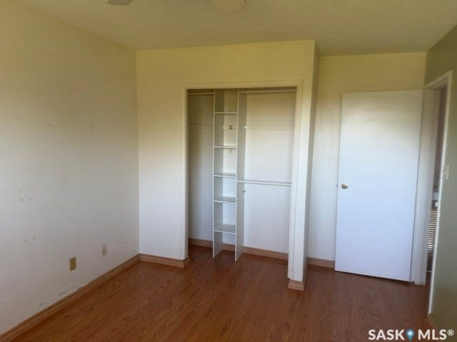 Wood-finish flooring with coordinating baseboards, a built-in closet with shelving and hanging rods, and a white ceiling fan