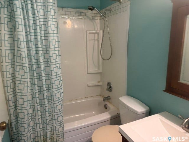 White tub with shower, white subway tile surround, white toilet, and a vanity with a white countertop and integrated sink