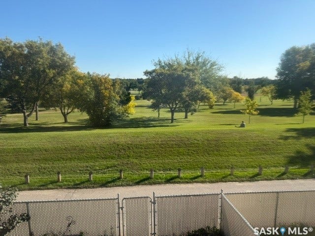 Expansive green space featuring mature trees and a paved pathway, bordered by a chain link fence