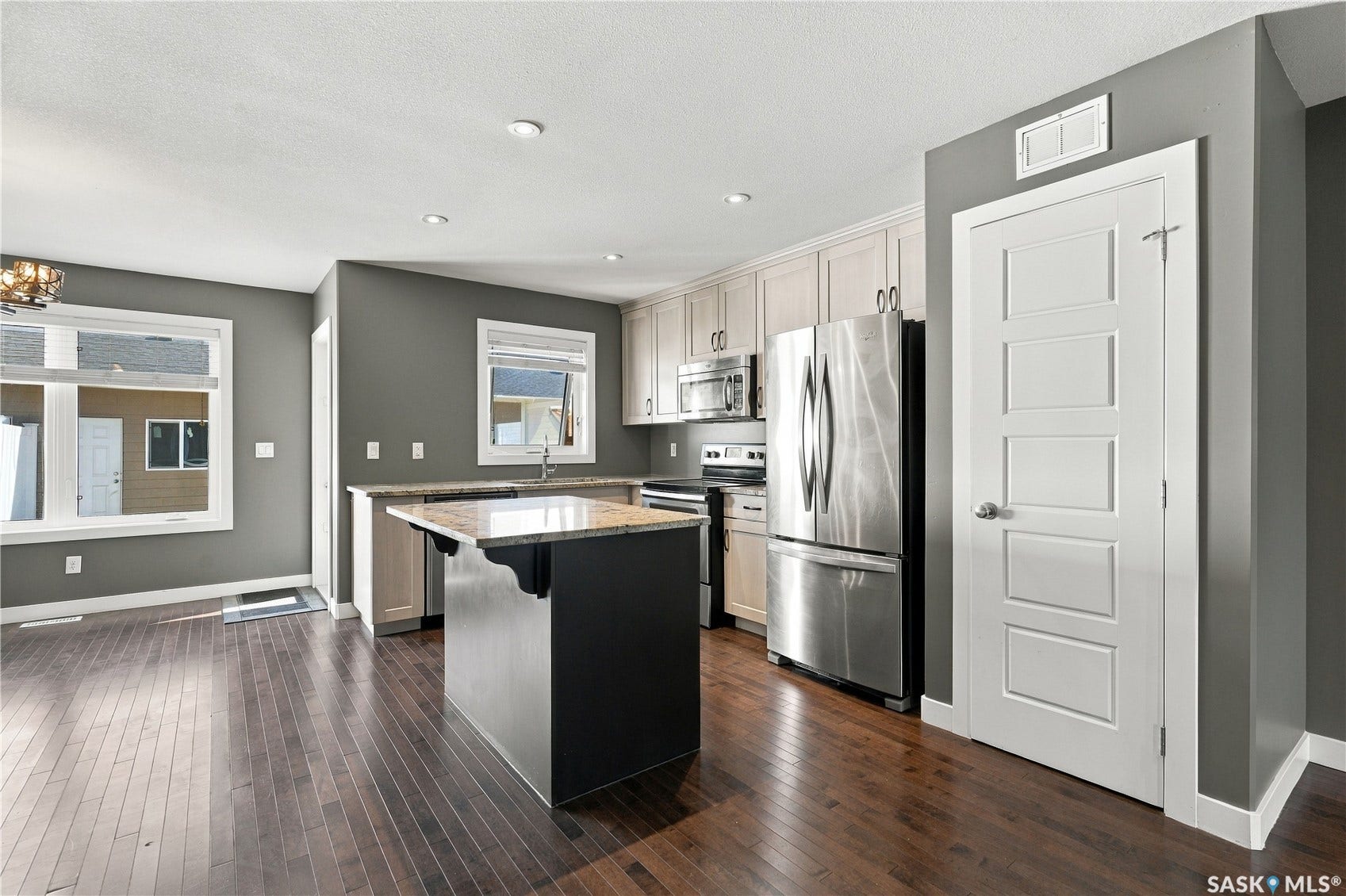 Hardwood flooring, kitchen island with stone countertop, stainless steel appliances, light wood-finish cabinetry, and recessed lighting