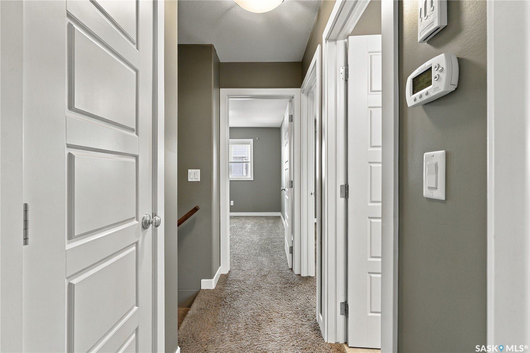 Hallway featuring paneled doors, carpet flooring, and a wall-mounted thermostat