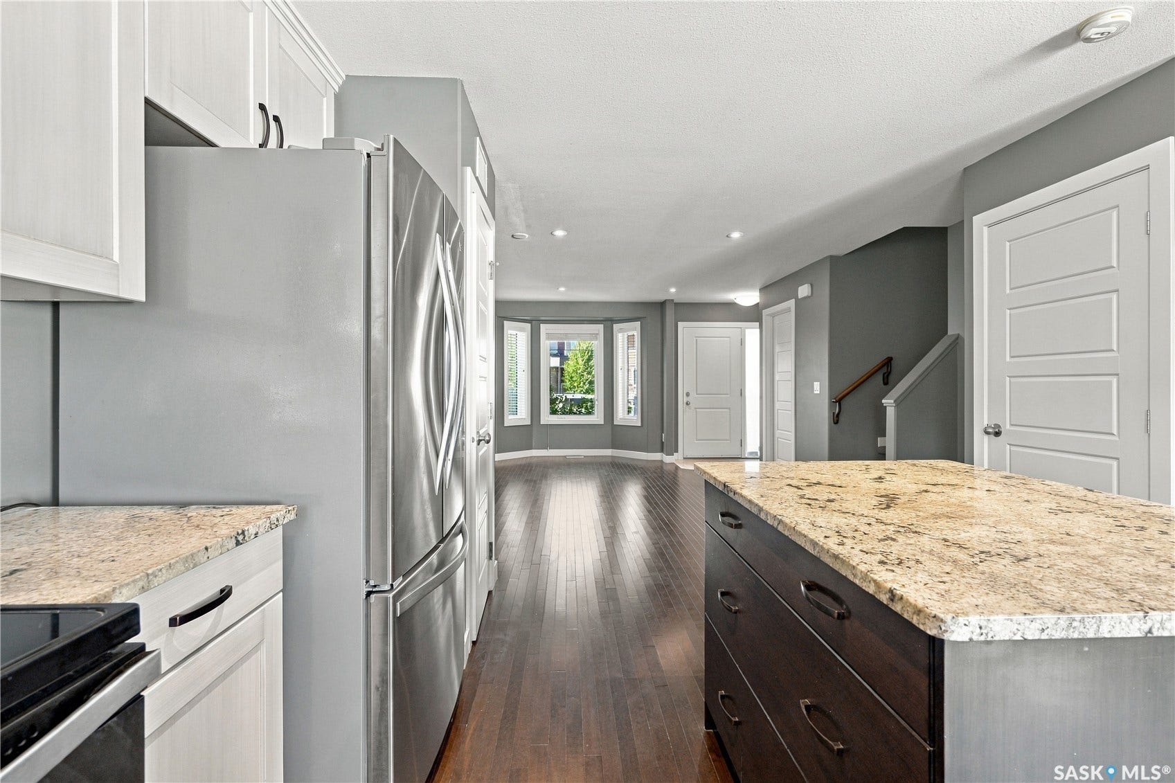 Chef's kitchen featuring stainless steel French-door refrigerator, white cabinetry with contrasting dark island base, granite countertops, and dark wood-finish flooring throughout