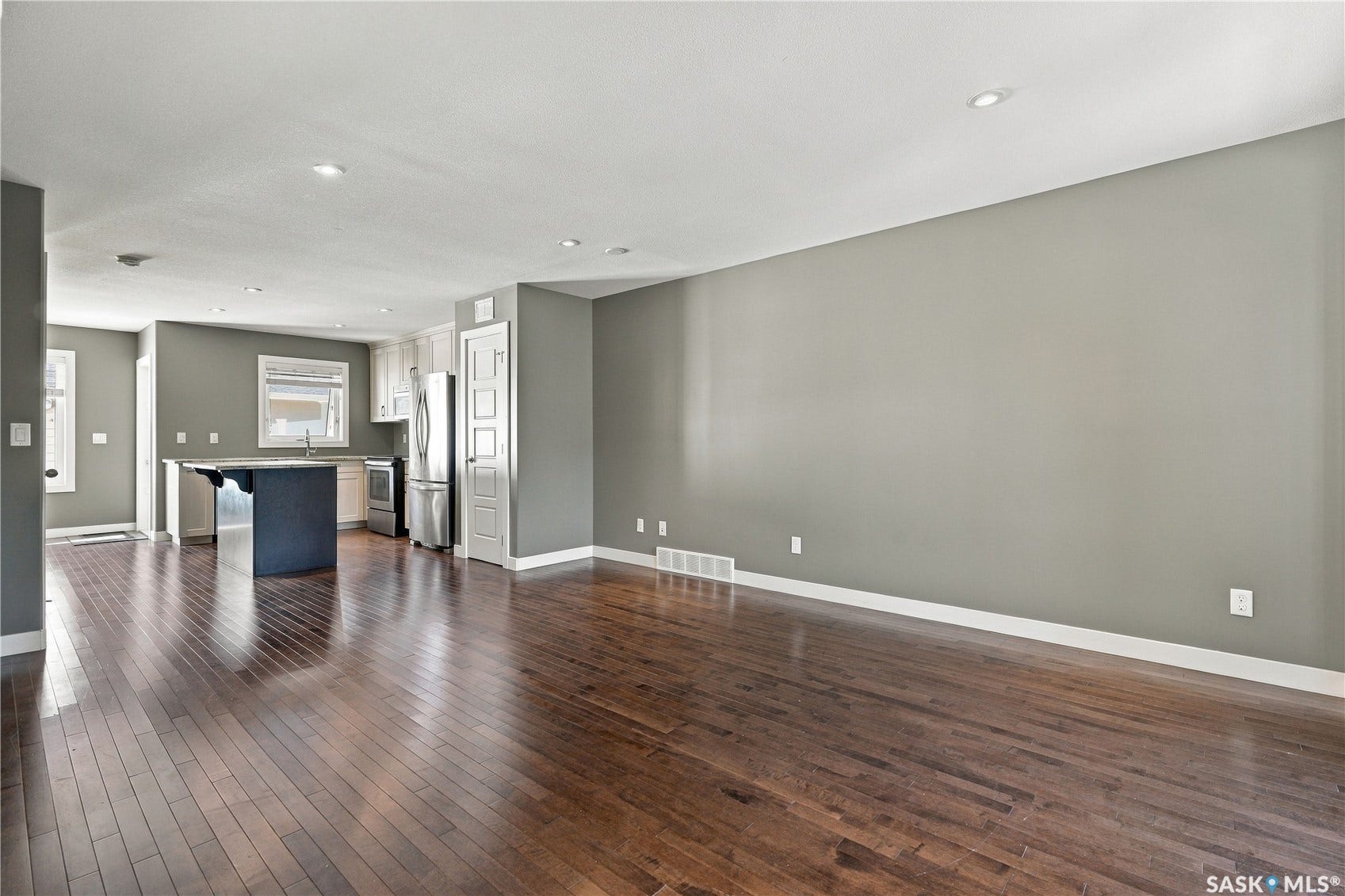 Open-concept layout featuring wood-finish flooring, recessed lighting, a kitchen island with seating, white cabinetry, and stainless steel appliances