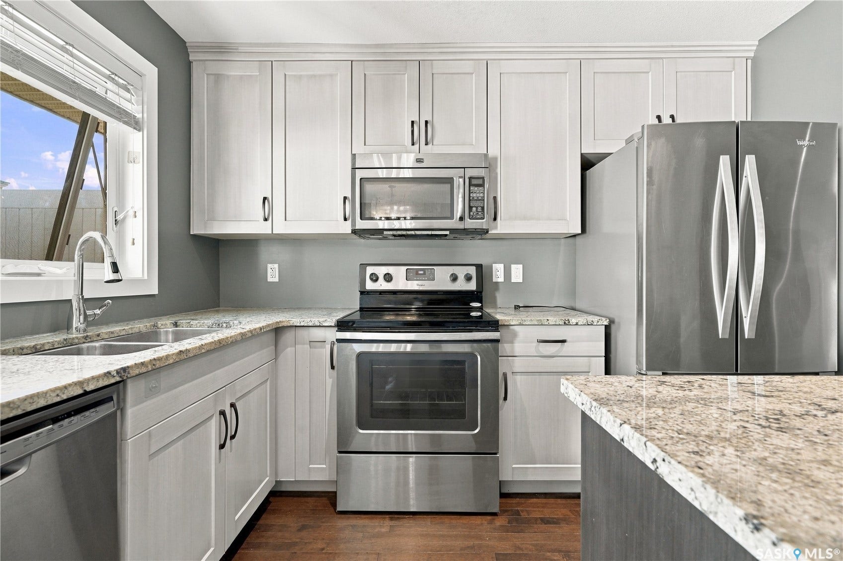 Stainless steel appliances, light-toned cabinetry, wood-finish flooring, and light-toned countertops