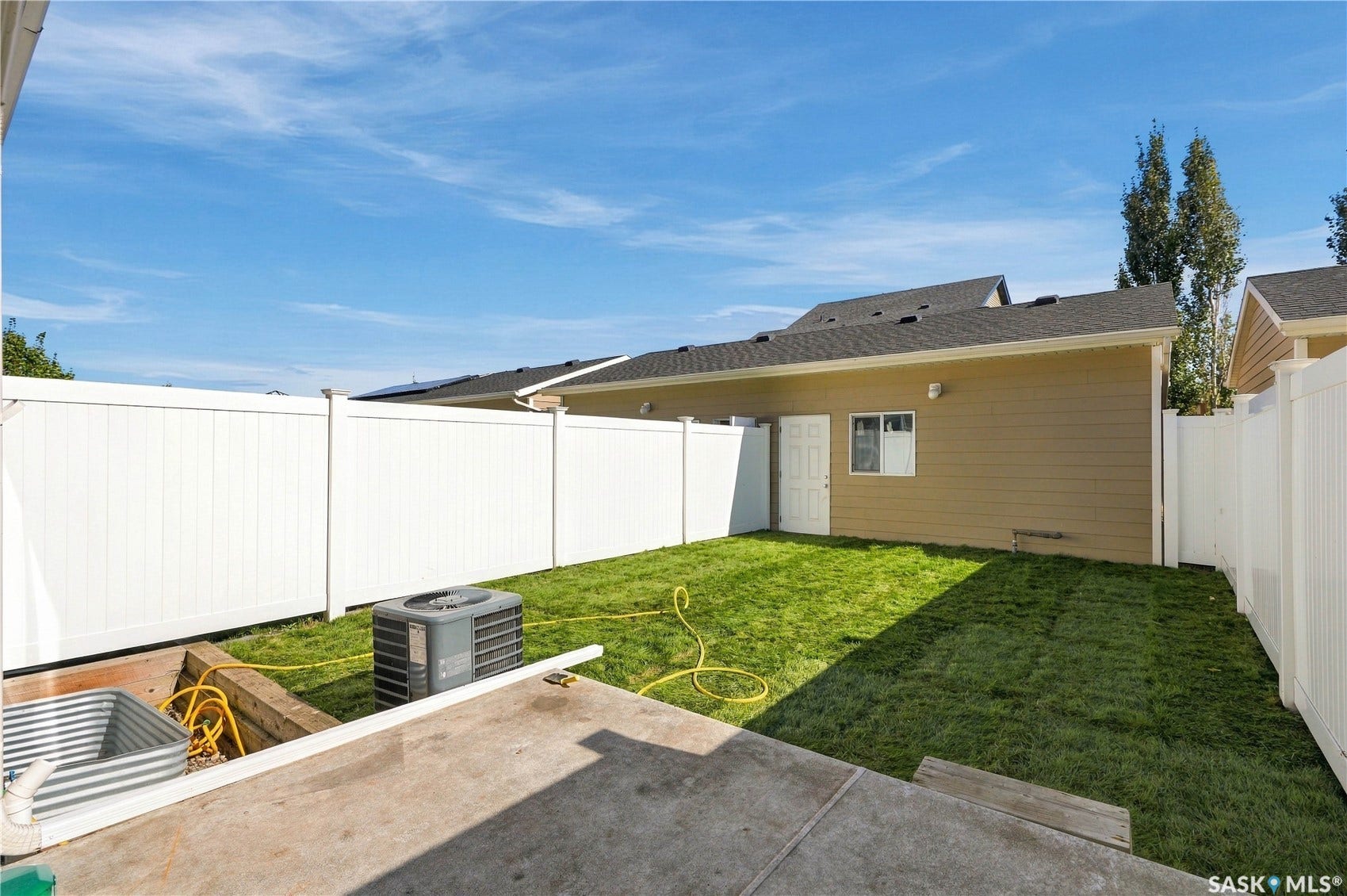 Grassed outdoor area with a concrete patio, vinyl fencing, and exterior building access