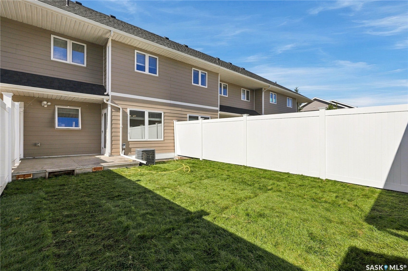 Expansive grassy yard with white privacy fencing, a concrete patio, and neutral-toned siding