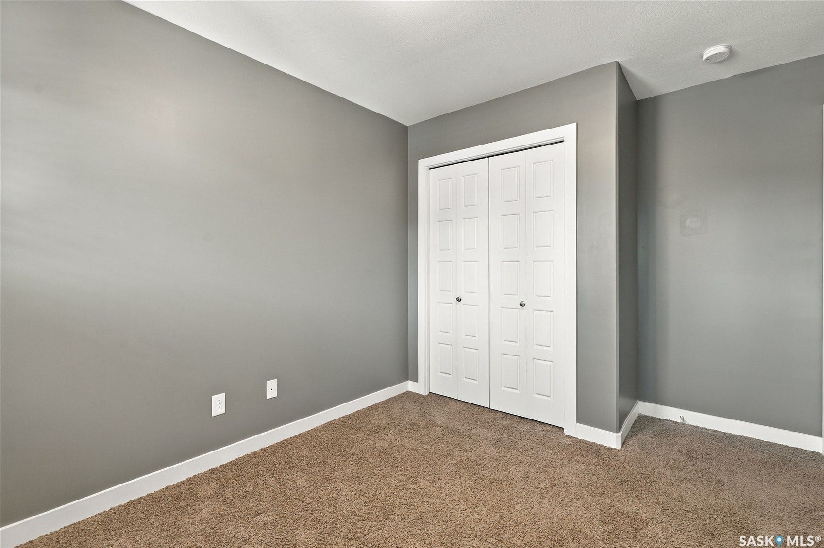 Neutral gray wall paint, white trim, brown carpeting, and a bi-fold closet door