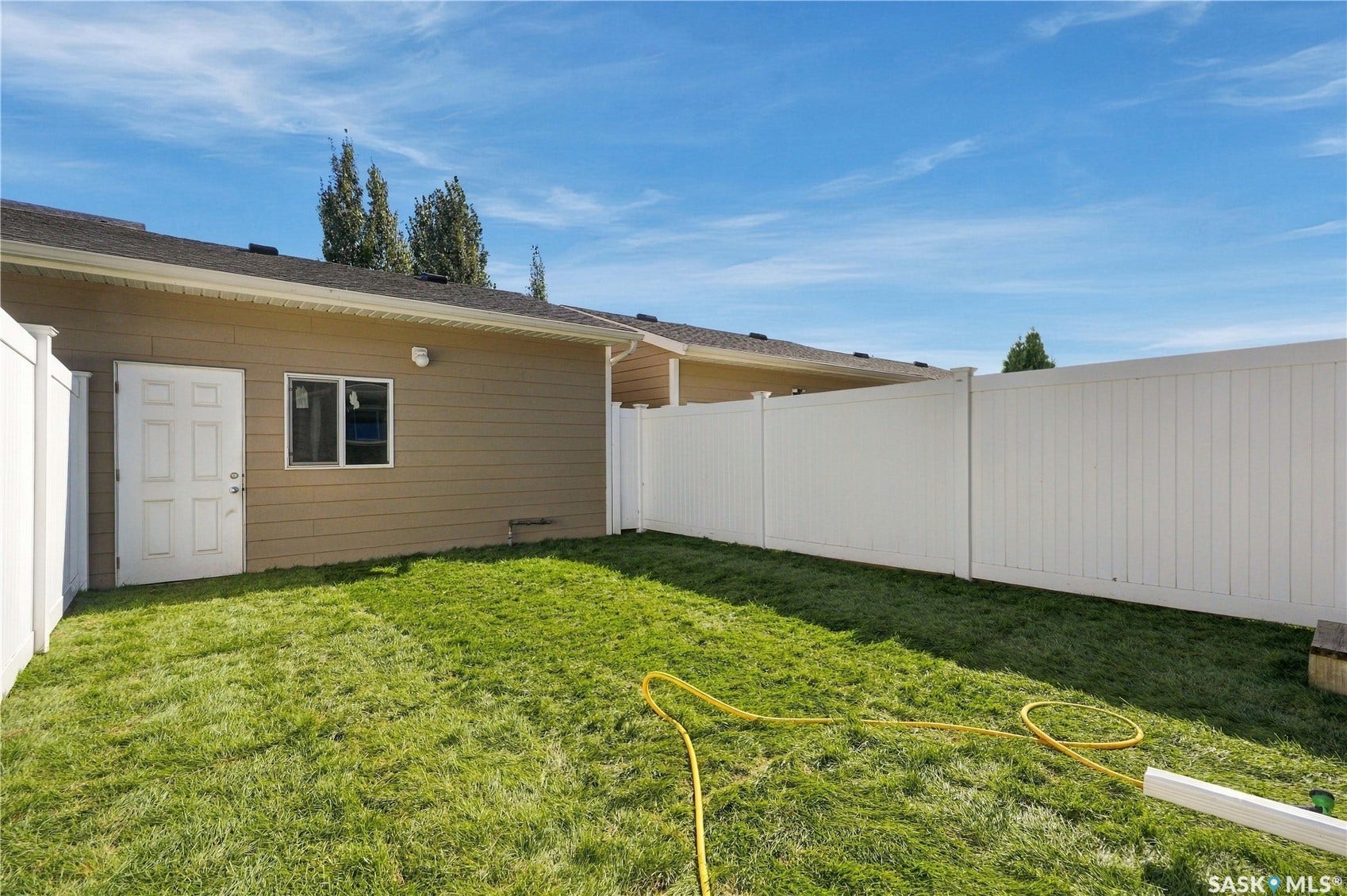 Expansive grassy area with a white privacy fence, a tan exterior wall, and a white exterior door
