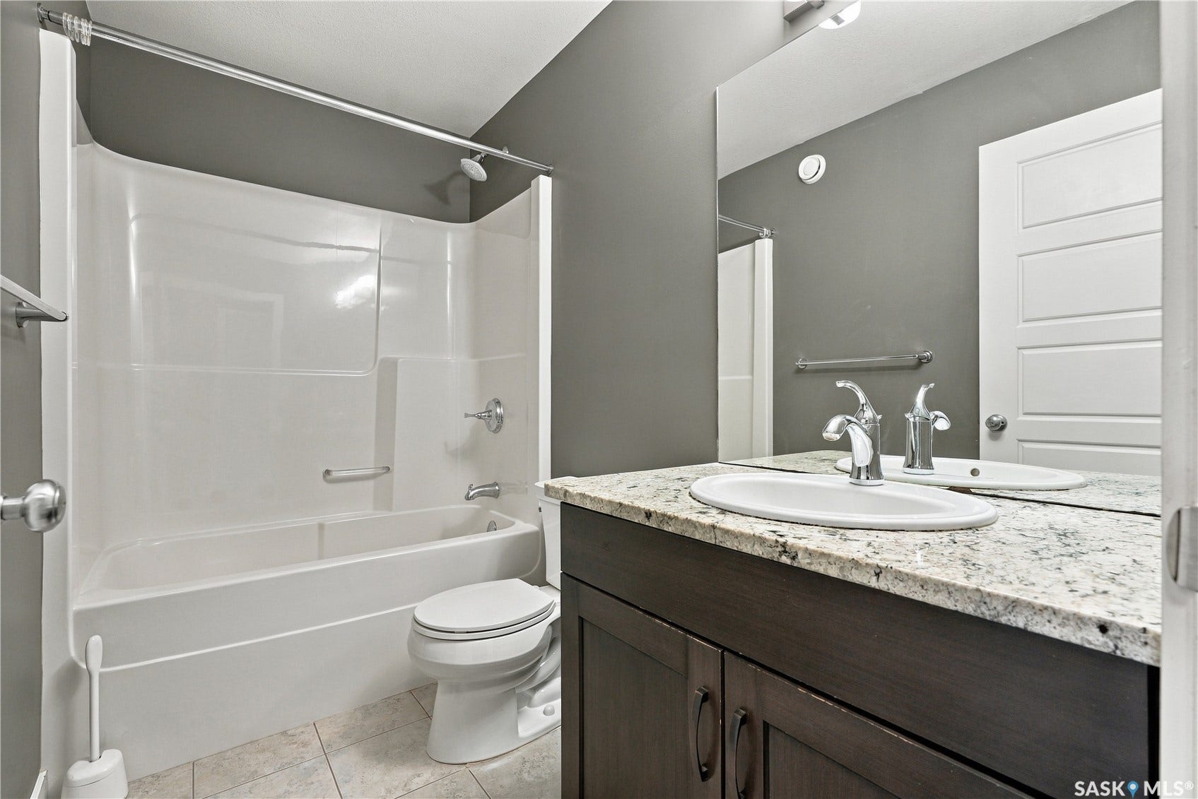 Bathroom featuring a vanity with a white countertop and oval sink, chrome faucet, wood-finish cabinetry, and a white shower-over-tub unit