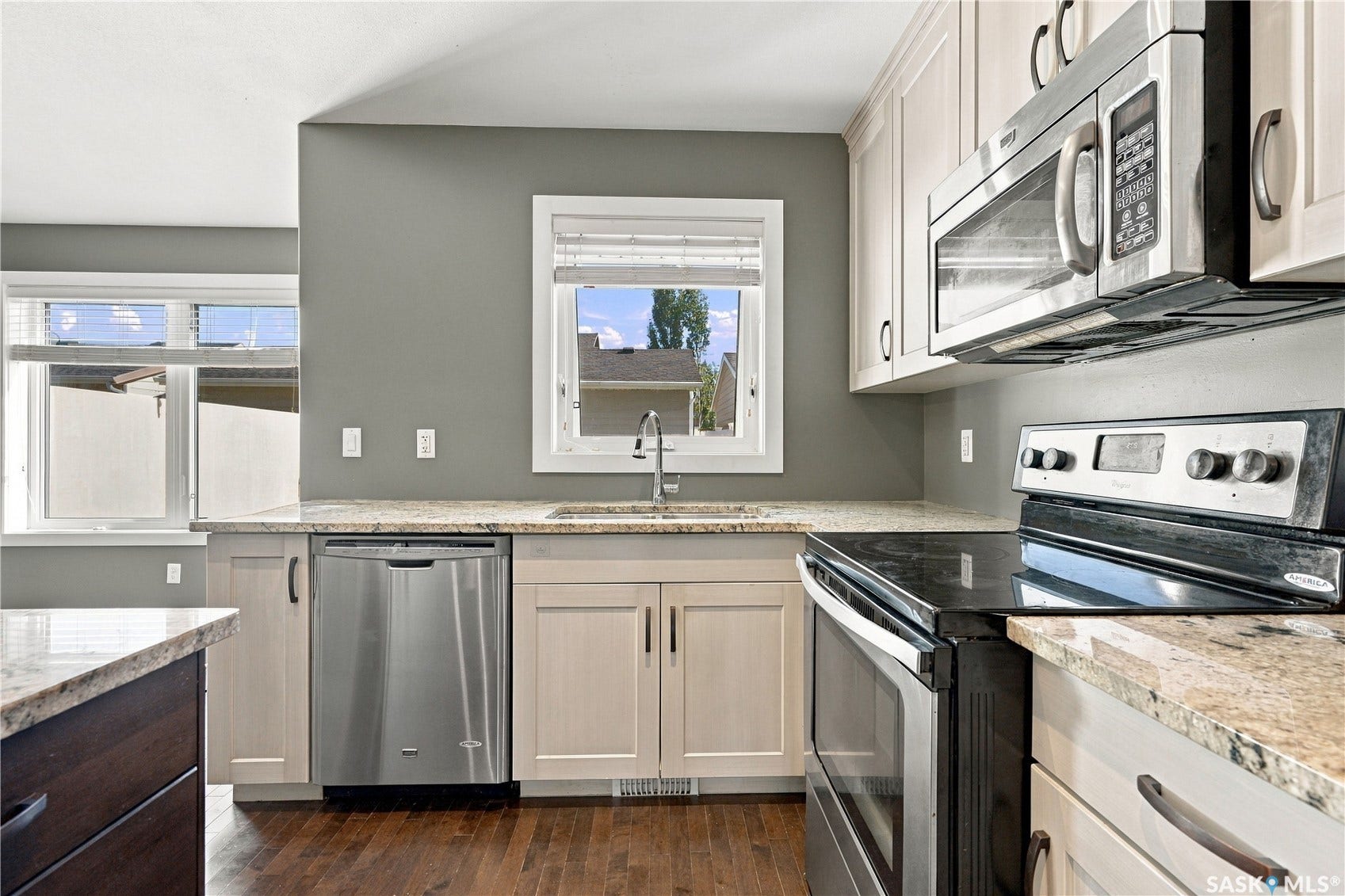 Kitchen featuring wood-finish flooring, light-toned cabinetry, stainless steel appliances, and stone countertops