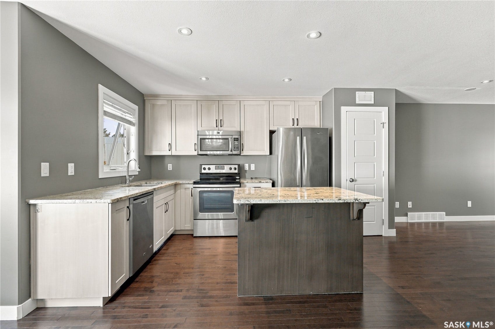 Contemporary kitchen featuring white cabinetry with stainless steel hardware, stainless steel appliances including a gas range and built-in microwave, granite countertops, a large center island with additional counter space, and wood-finish flooring throughout the open-concept layout
