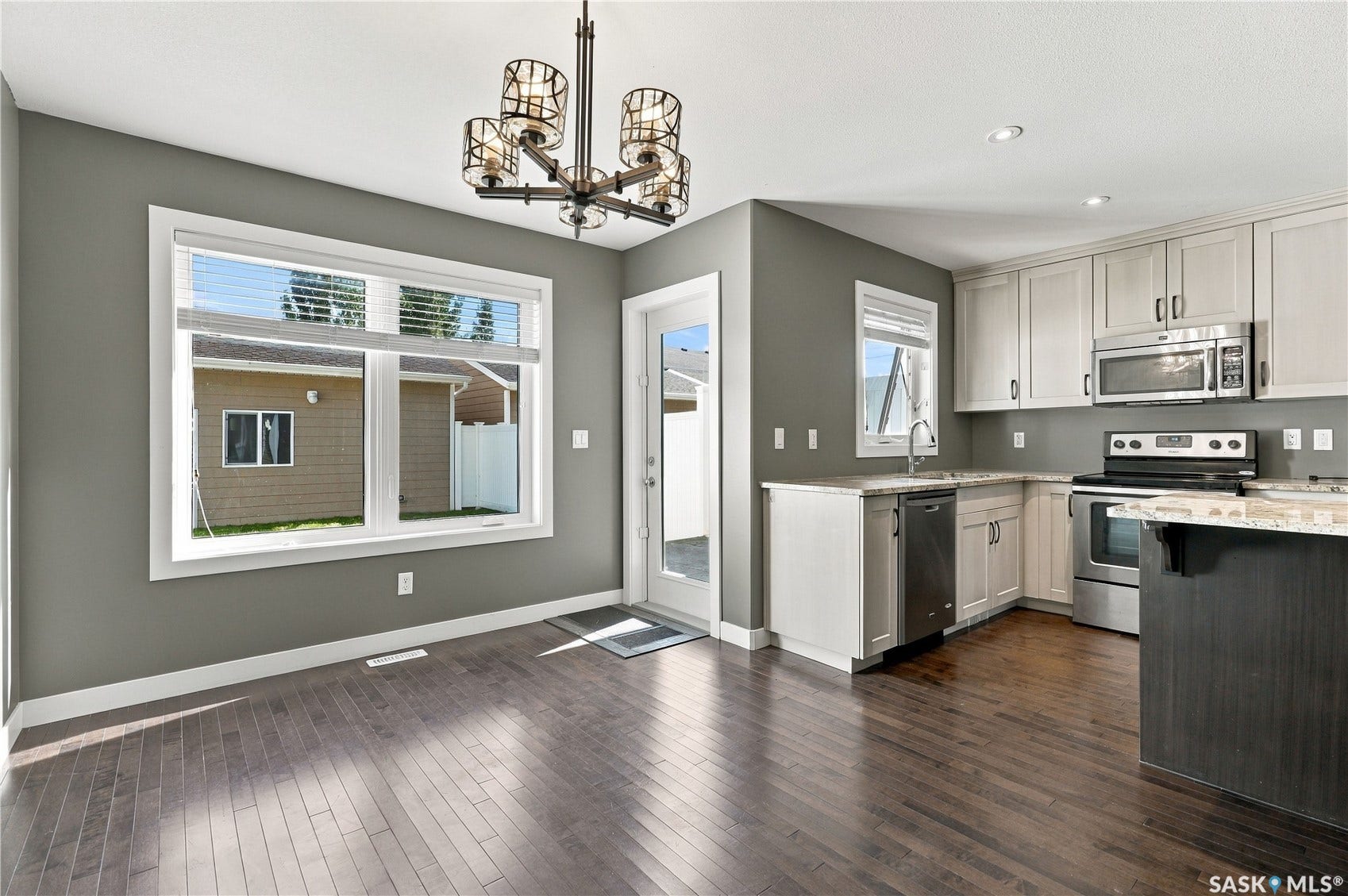 Wood-finish flooring, contemporary chandelier, large picture window, white baseboards, and stainless steel appliances