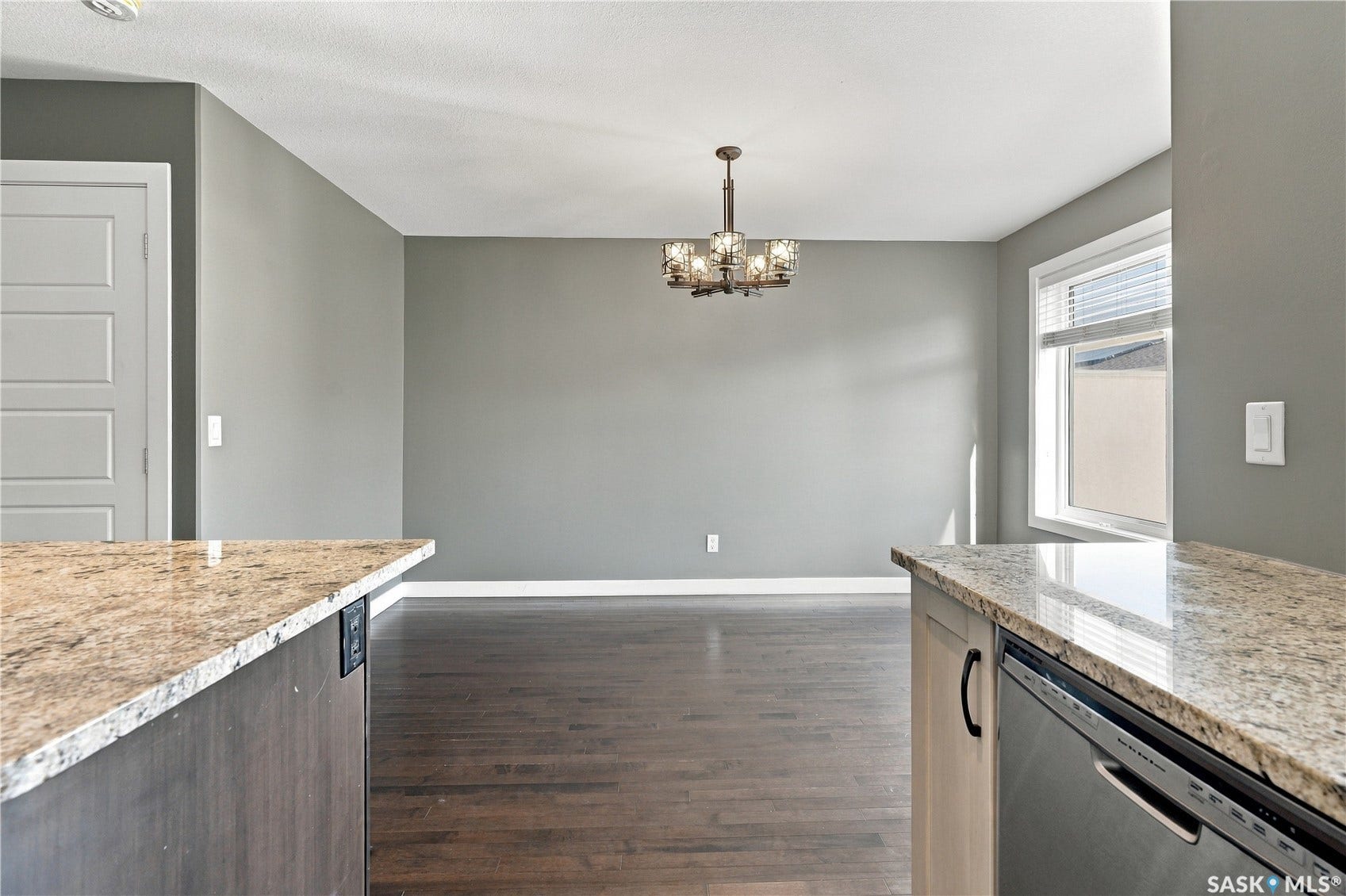 Spacious interior featuring a contemporary chandelier, durable wood-finish flooring, and a bright window with blinds