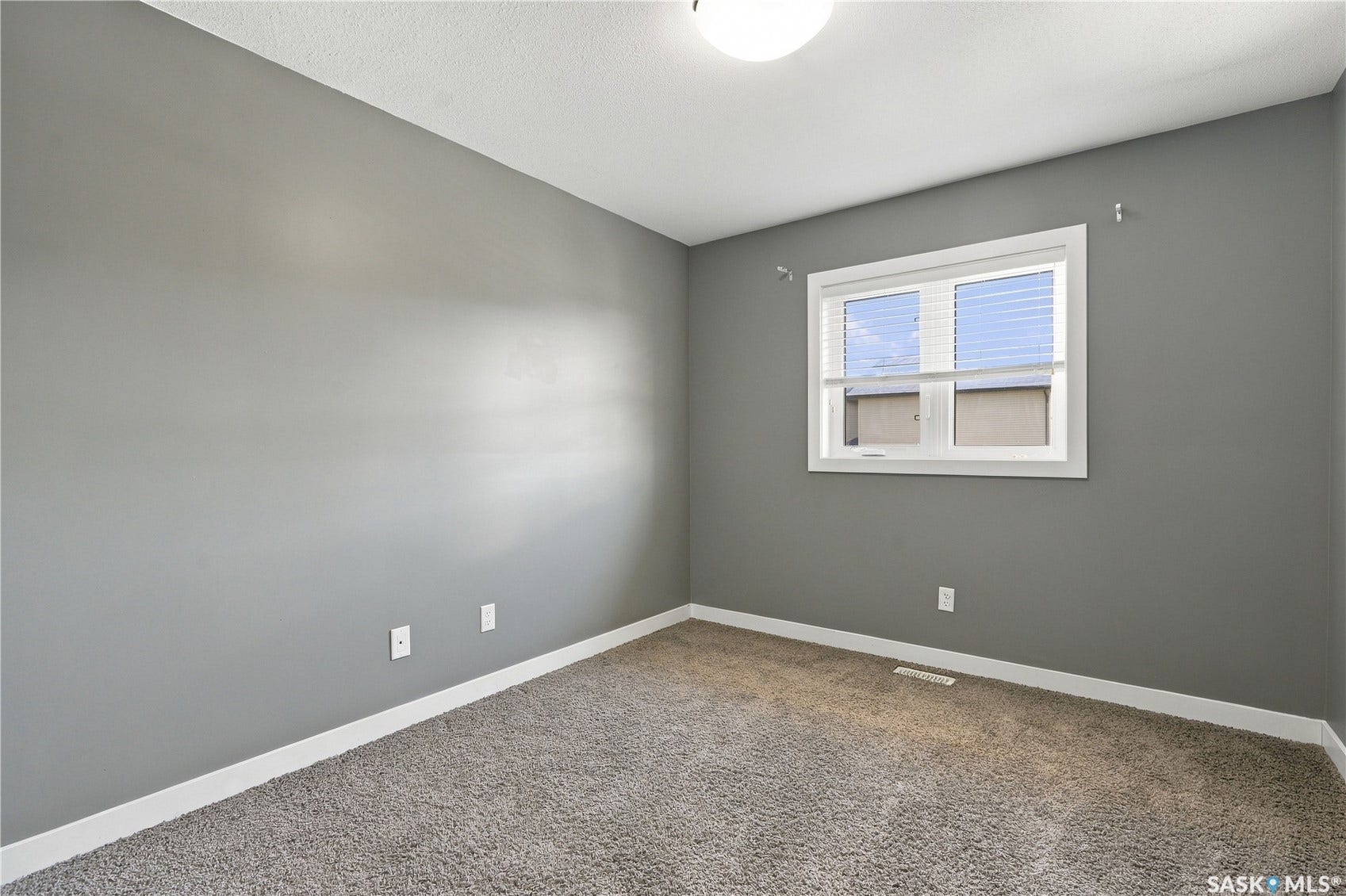 Neutral gray walls with white trim, window with blinds, and textured gray carpeting