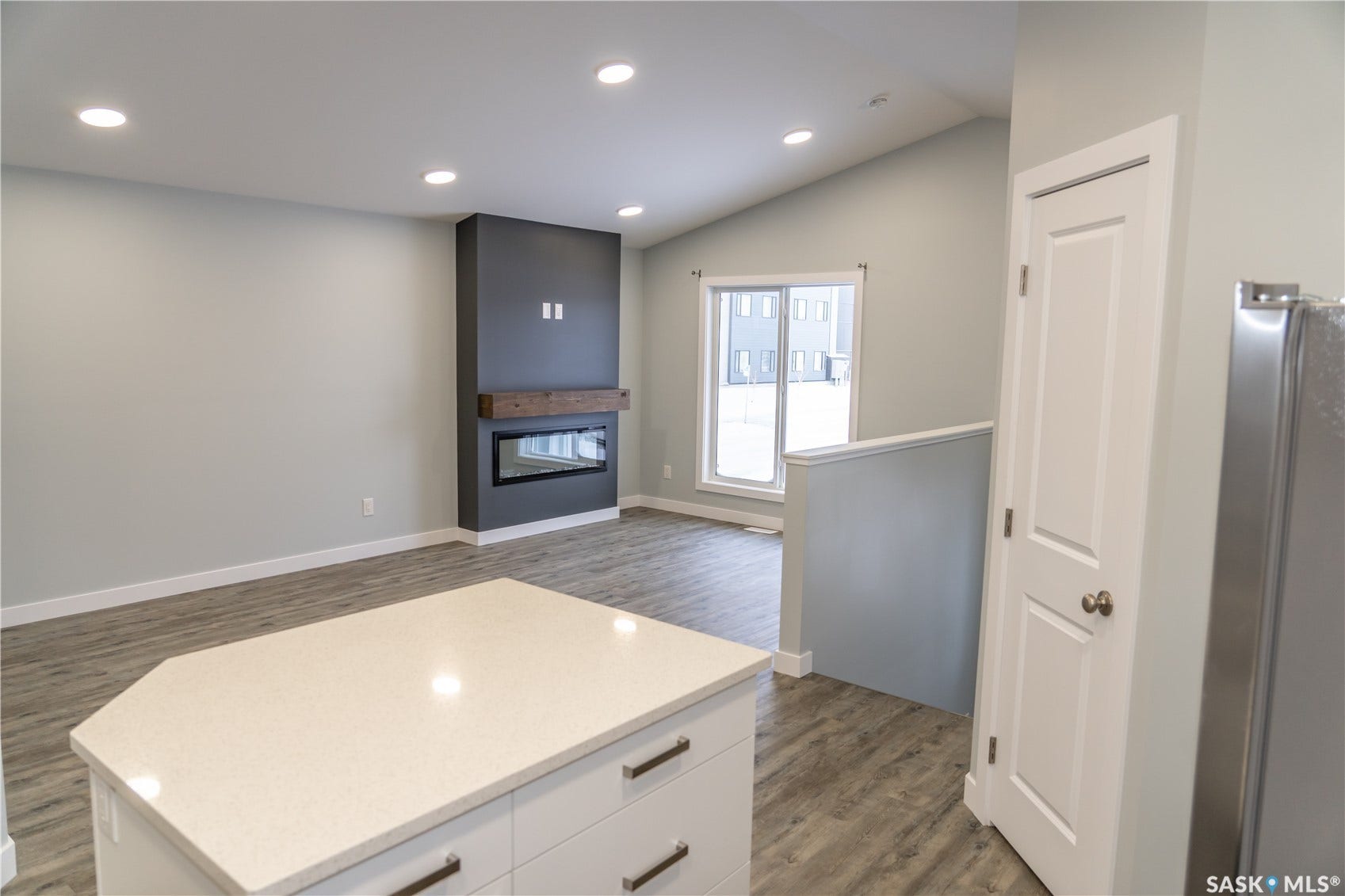 306 Stehwien Street, Saskatoon SK S7W 1P3 Kitchen with dark wood-type flooring, light stone counters, stainless steel fridge, vaulted ceiling, and white cabinetry